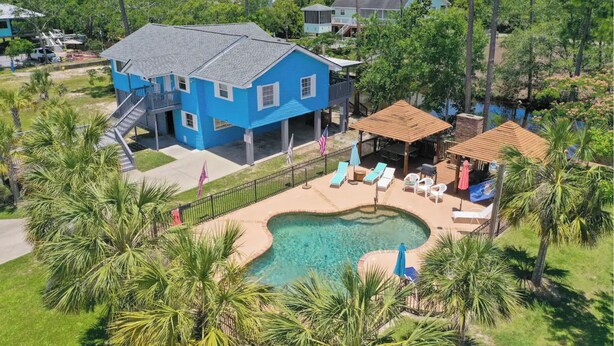 Une maison bleue avec une piscine, entourée de palmiers et dotée d’un patio couvert.