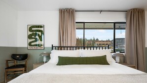 A hotel room with a large bed, a chair, a nightstand, and a window with curtains. - Luxury Harbor Escape | Walk to Food & Fun (Juneau)