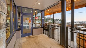 A covered outdoor area with a glass door leading to a restaurant, a view of a marina, and a stone wall on the left. - Luxury Harbor Escape | Walk to Food & Fun (Juneau)