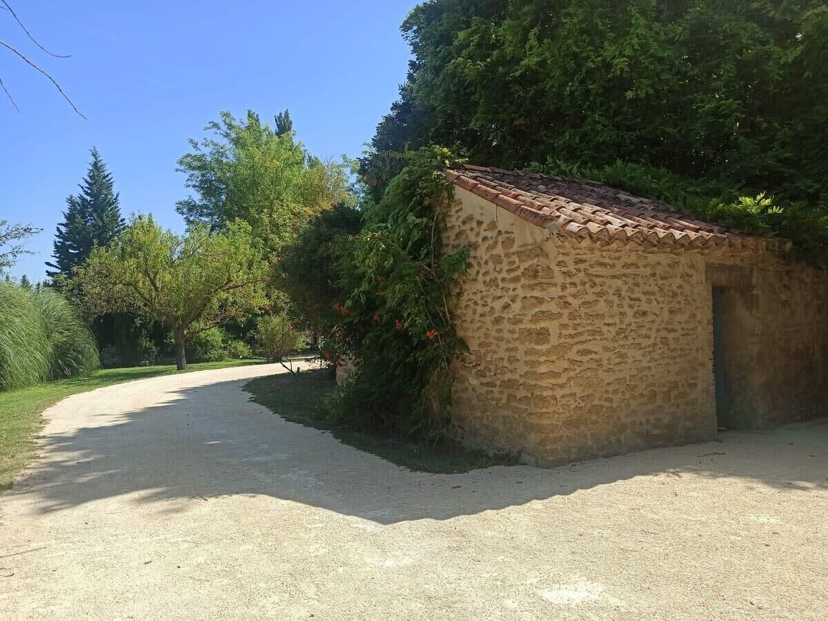 Un camino de grava que conduce a un edificio de piedra con techo de tejas, rodeado de vegetación y árboles.