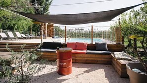 Un espace aménagé au bord de la piscine, avec une terrasse en bois, un coin salon doté de coussins, un hamac et un petit tonneau portant l’inscription « FRUCTA ».