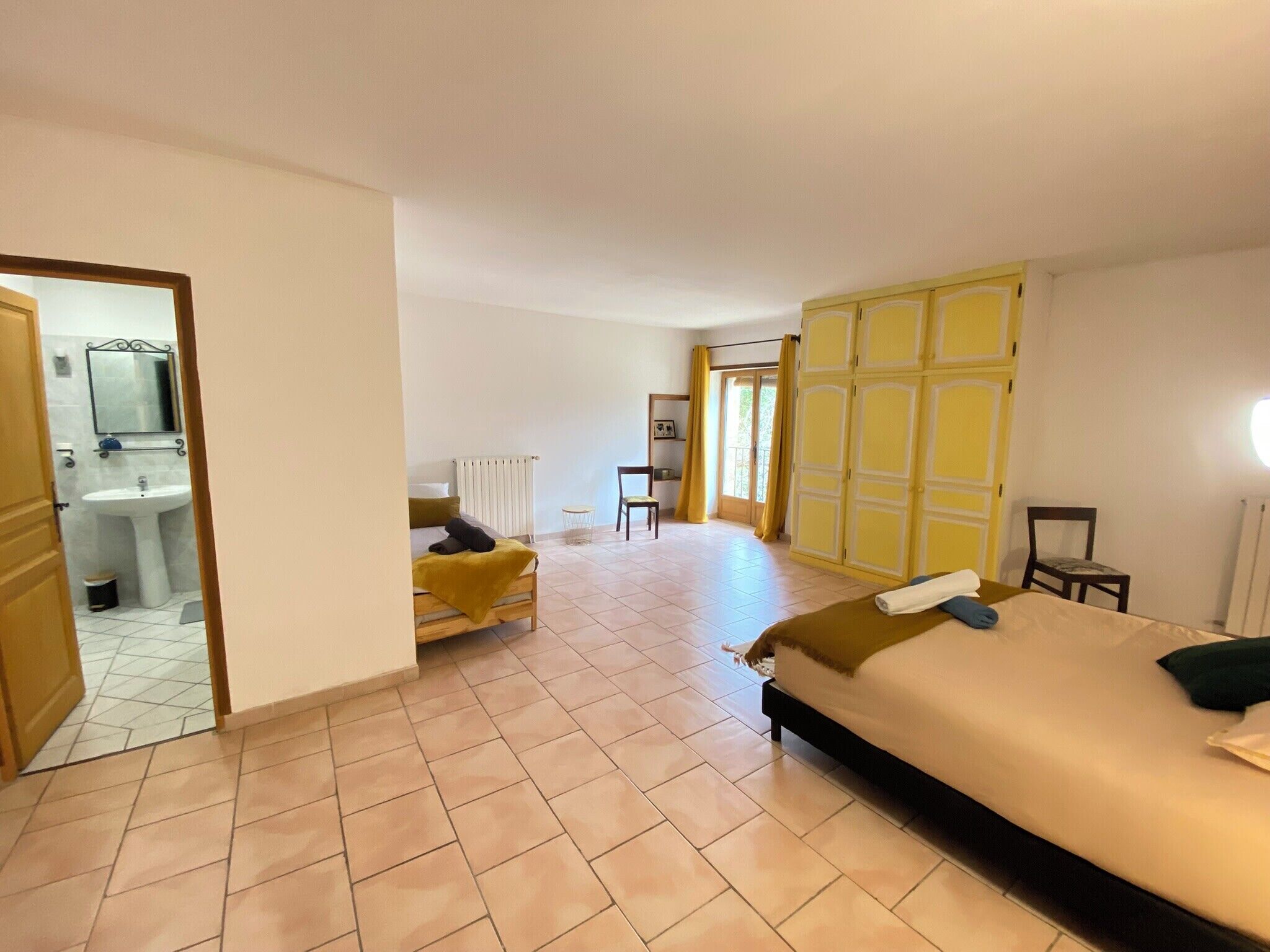 Habitació d'hotel amb un llit, una cadira, una taula petita, un mirall i un bany amb un lavabo i un vàter.