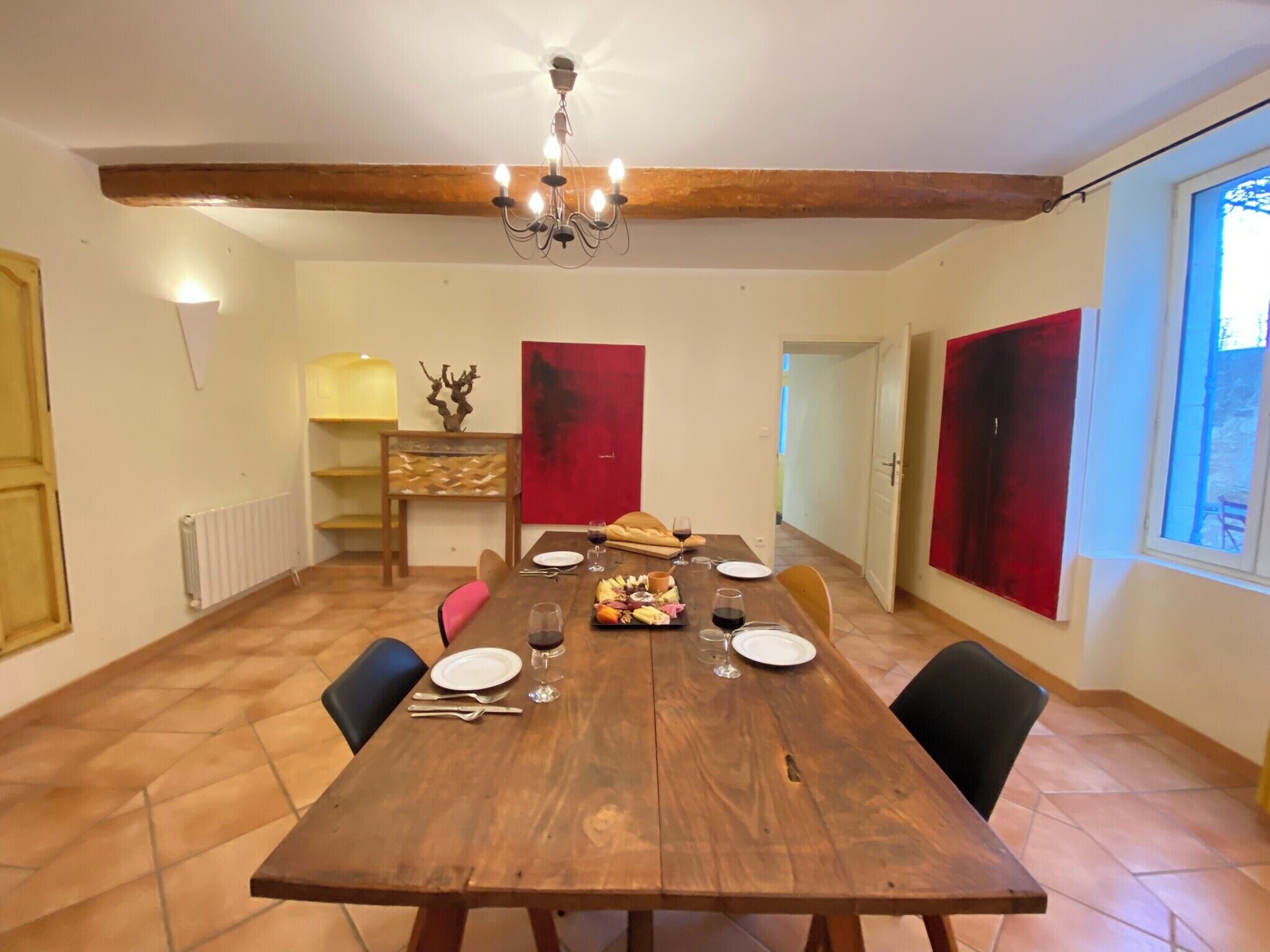 A dining room with a wooden table set for four, a chandelier, and red curtains.