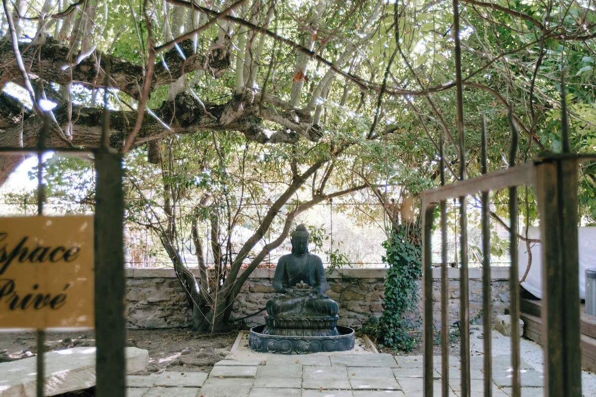 Une statue de Bouddha dans un jardin, avec un banc en pierre et une pancarte indiquant « Espace privé ».