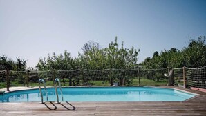 Une terrasse en bois avec une piscine, entourée d’une clôture en filet et d’arbres.