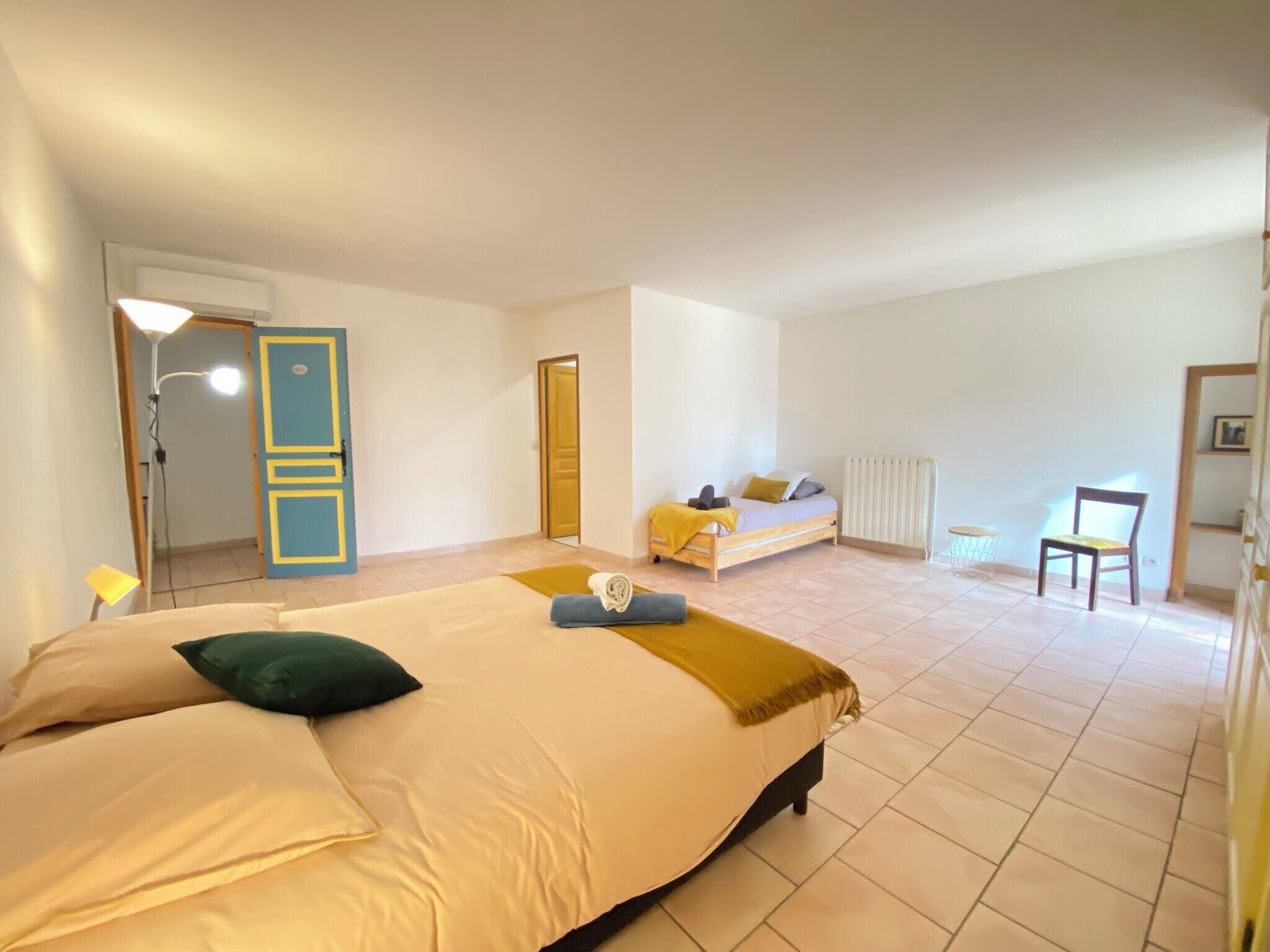 Een ruime slaapkamer met een groot bed, een kleiner bed, een stoel en een radiator.
