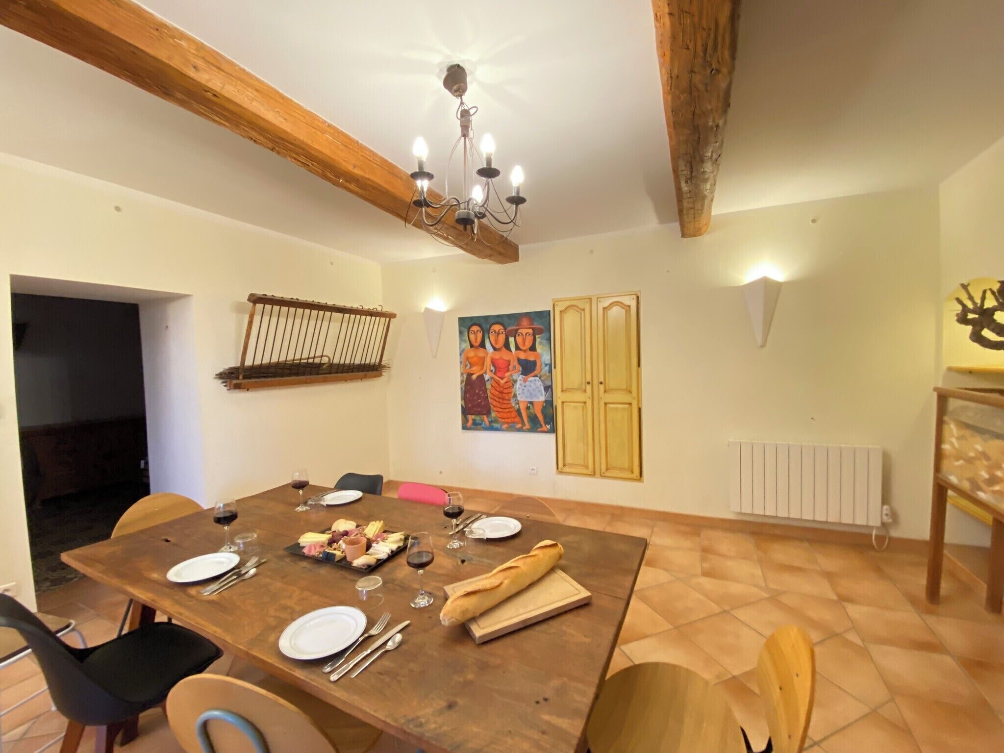 A dining area with a wooden table set for a meal, a chandelier, and a painting on the wall.