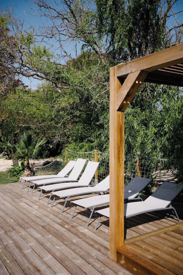 A wooden deck with white lounge chairs and a wooden pergola.