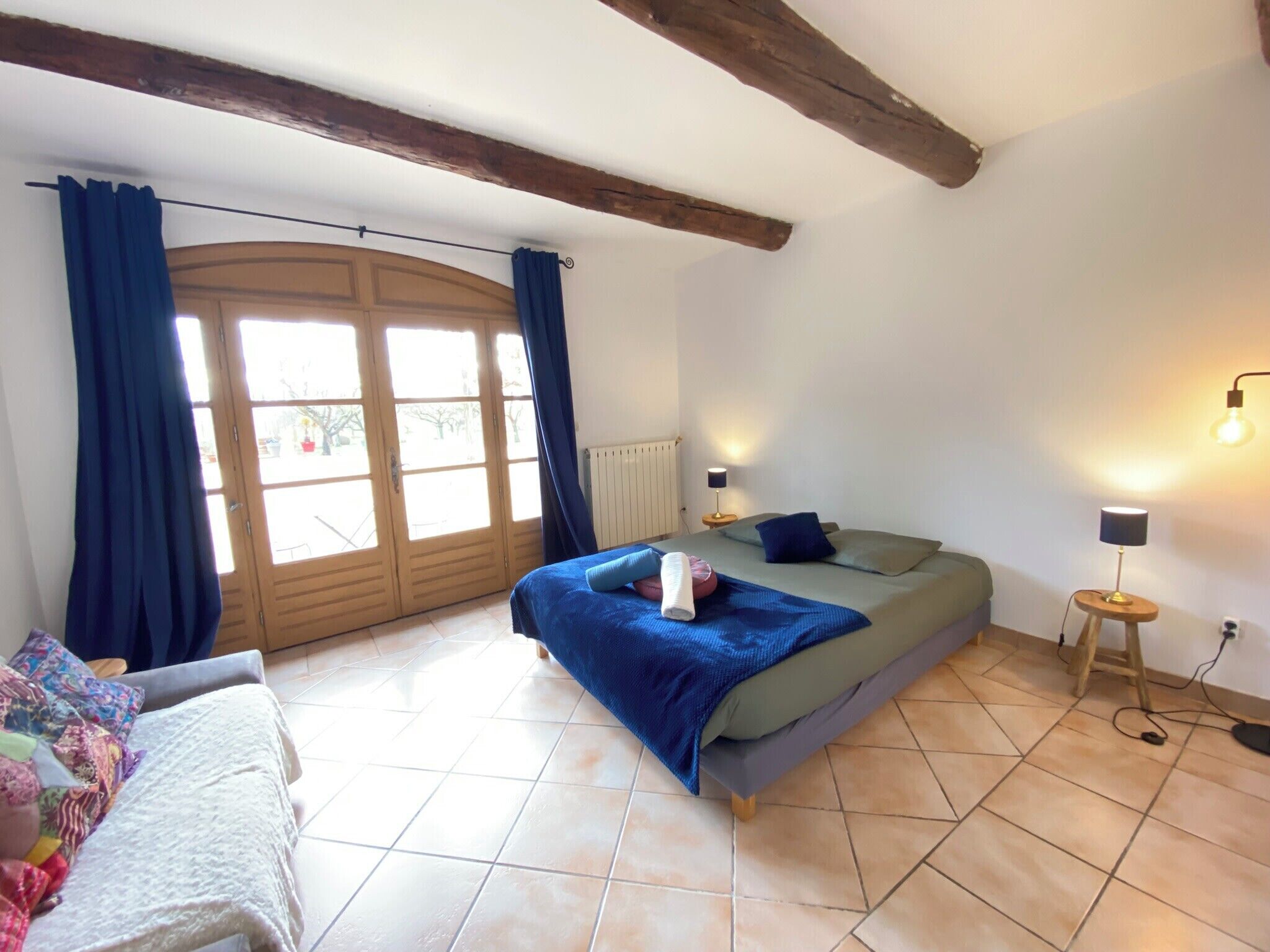 A bedroom with a bed, a window with curtains, a radiator, and a lamp.