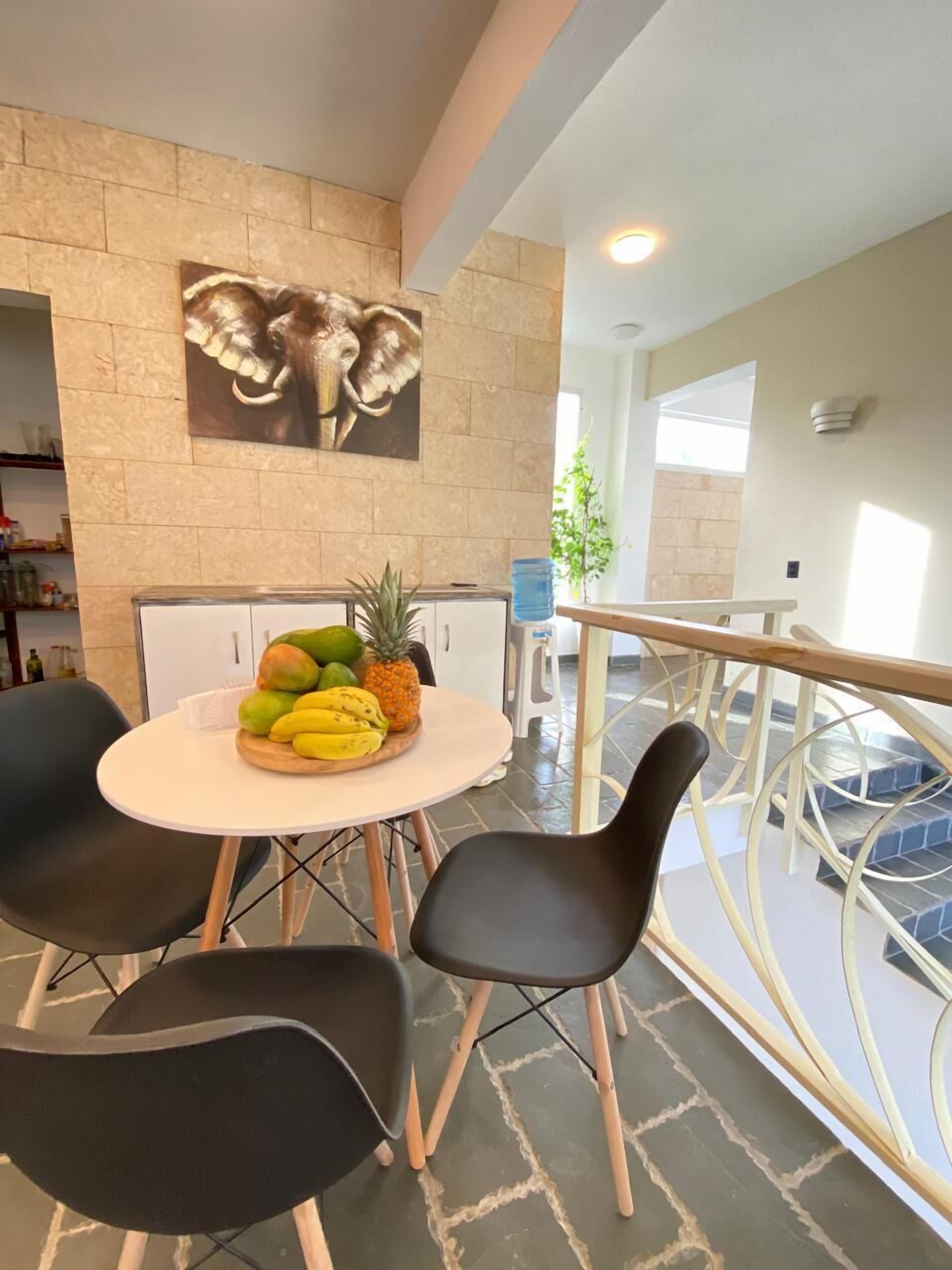 A modern dining area with a round table, black chairs, and a fruit bowl.
