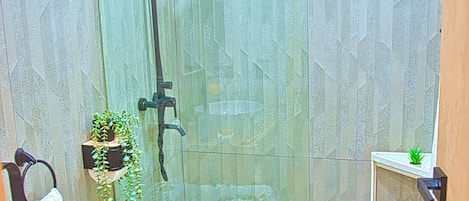 A modern bathroom with a glass-enclosed shower, a toilet, a sink, and a small shelf with plants.