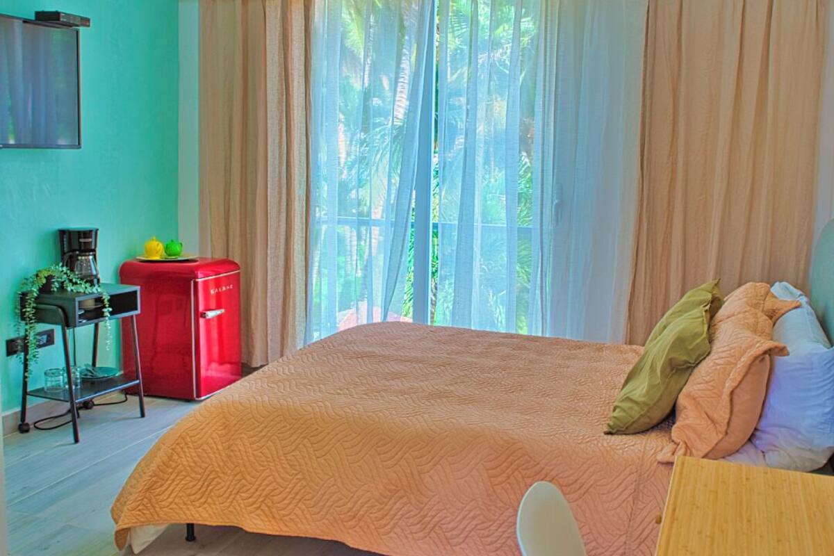 A bedroom with a bed, a desk, a chair, a ceiling fan, and an air conditioning unit.