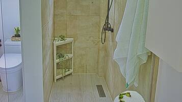 Une salle de bain avec une douche, une petite étagère avec des plantes, une baignoire blanche et un lavabo blanc.