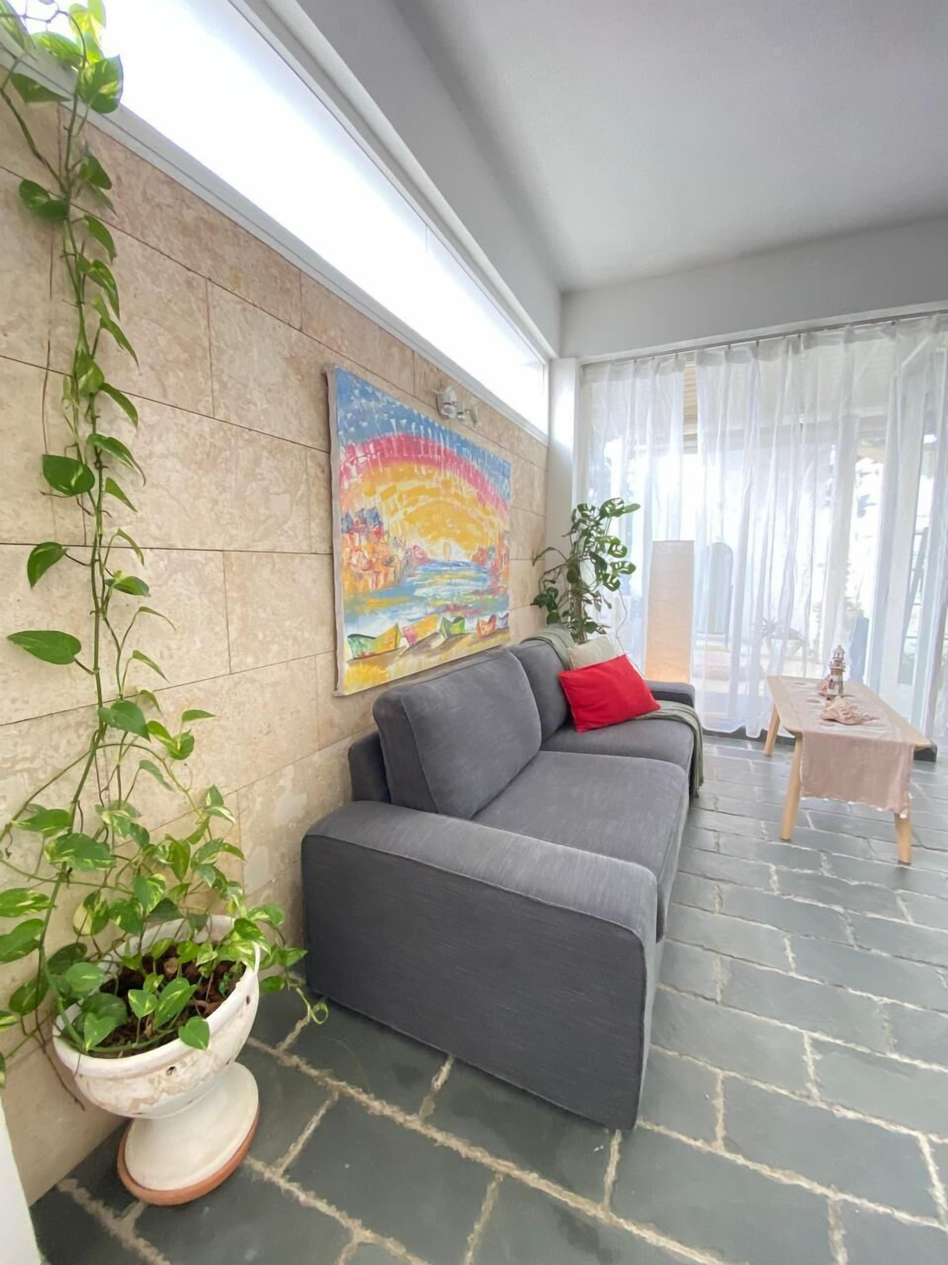 A modern living room with a grey sofa, a red pillow, a painting of a rainbow, and a potted plant.