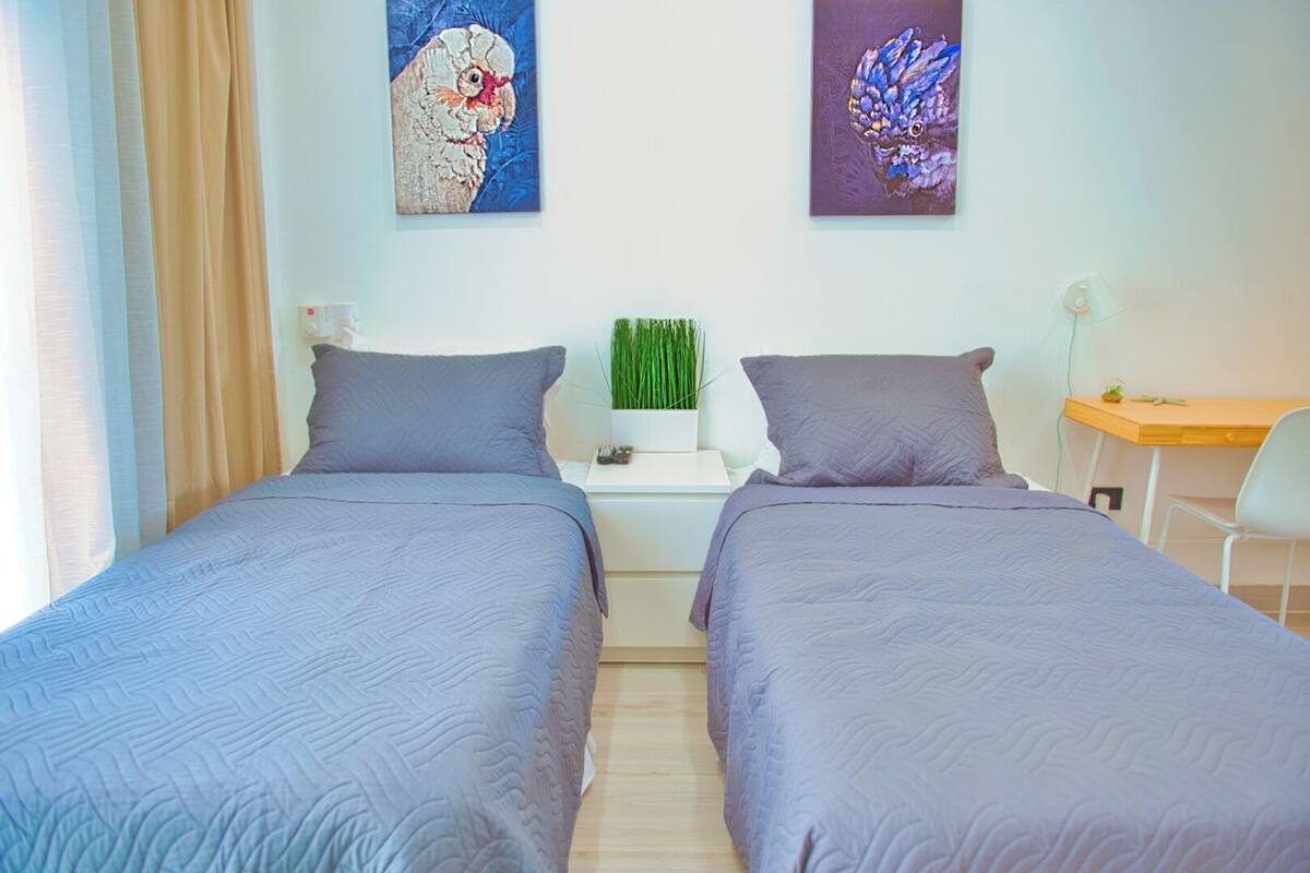 A double room with two beds, a small desk, and a chair. There are two paintings on the wall.