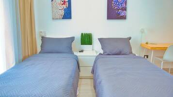 A double room with two beds, a small desk, and a chair. There are two paintings on the wall.