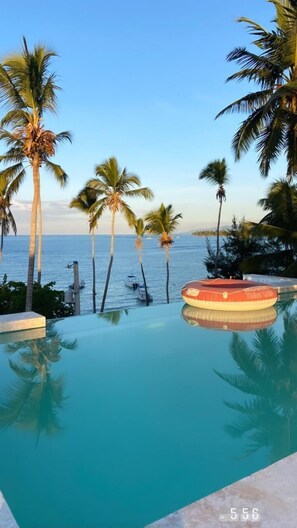 A pool with clear blue water, surrounded by palm trees and a view of the ocean.