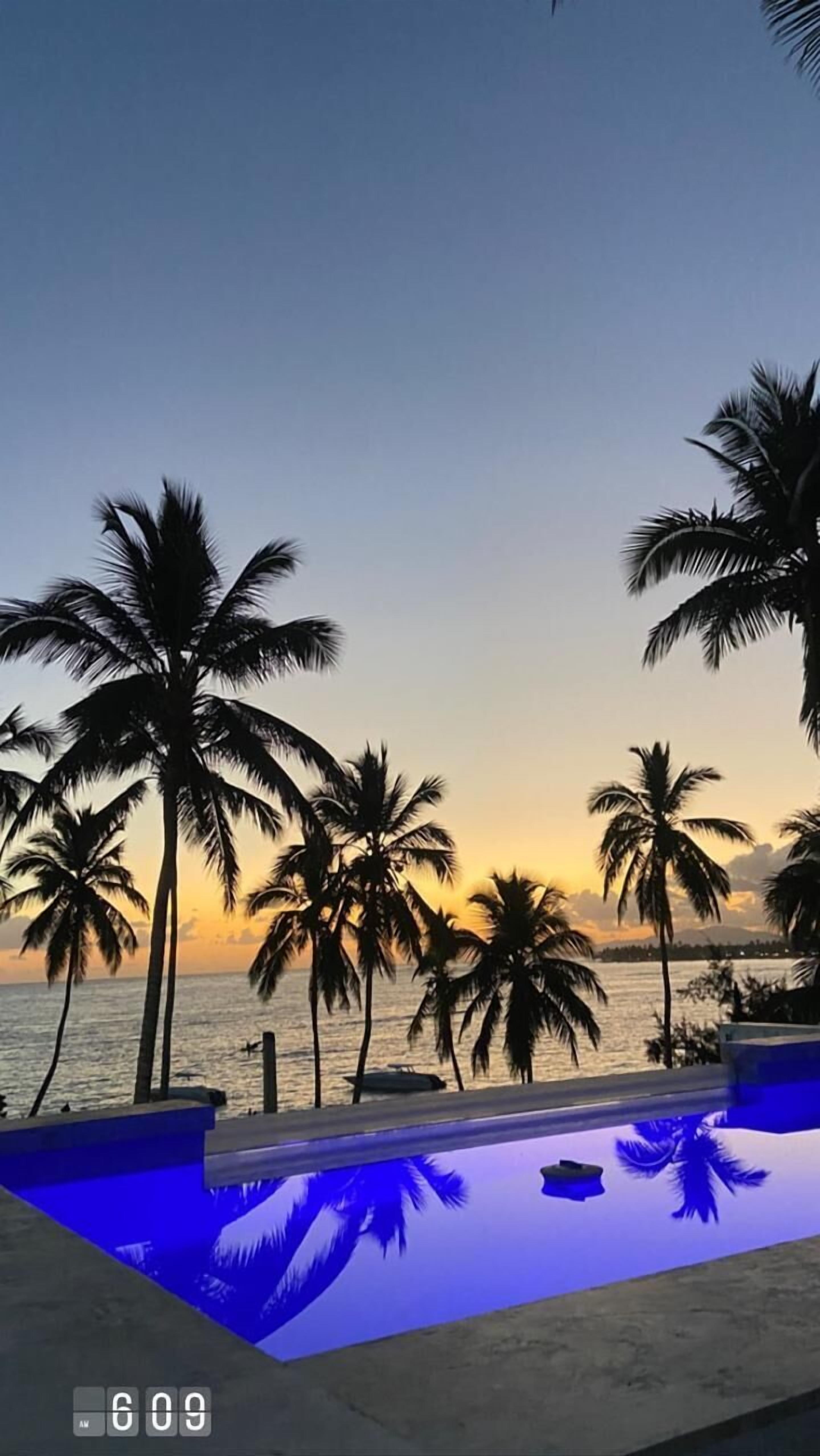 Zona de piscina con palmeras y vistas al atardecer.