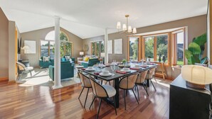 Un vaste espace dédié à la salle à manger, avec une longue table dressée pour le repas, entouré de sièges confortables et de grandes fenêtres offrant une vue sur l’extérieur.