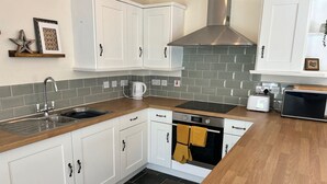 A modern kitchen with white cabinets, a stainless steel range hood, a built-in oven, a microwave, and a sink with a faucet.