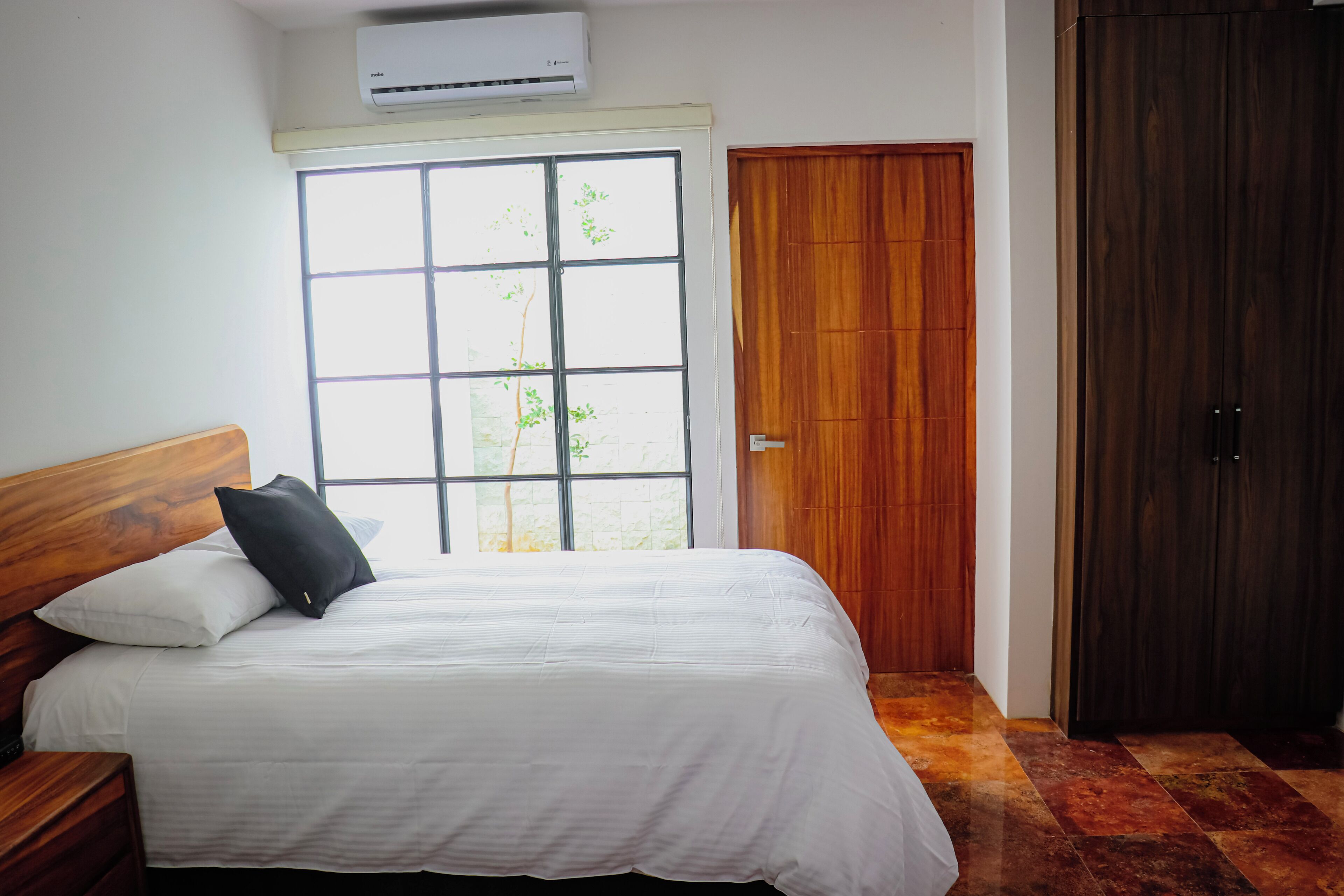 Un dormitorio con un ventanal grande, un armario de madera y una cama con ropa blanca.