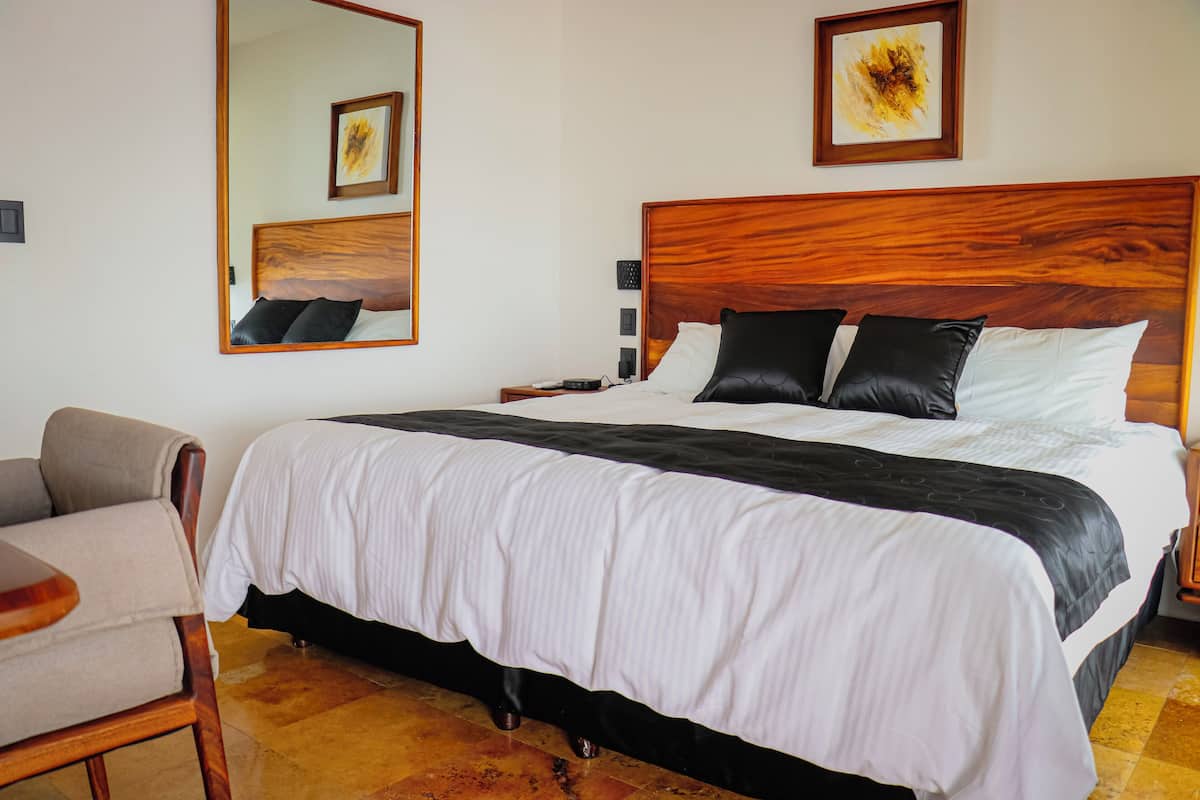 A hotel room with a large bed, a wooden headboard, a chair, and a nightstand.
