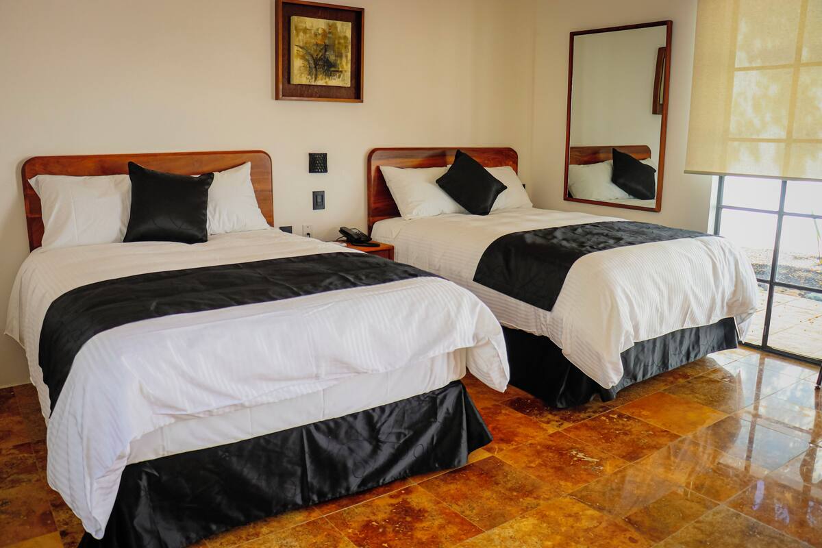 A hotel room with two beds, a large mirror, and a window with a view.