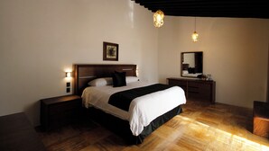 A bedroom with a bed, bedside tables, a nightstand, a mirror, and a hanging light fixture. - Hotel Casa María  (Oaxaca)