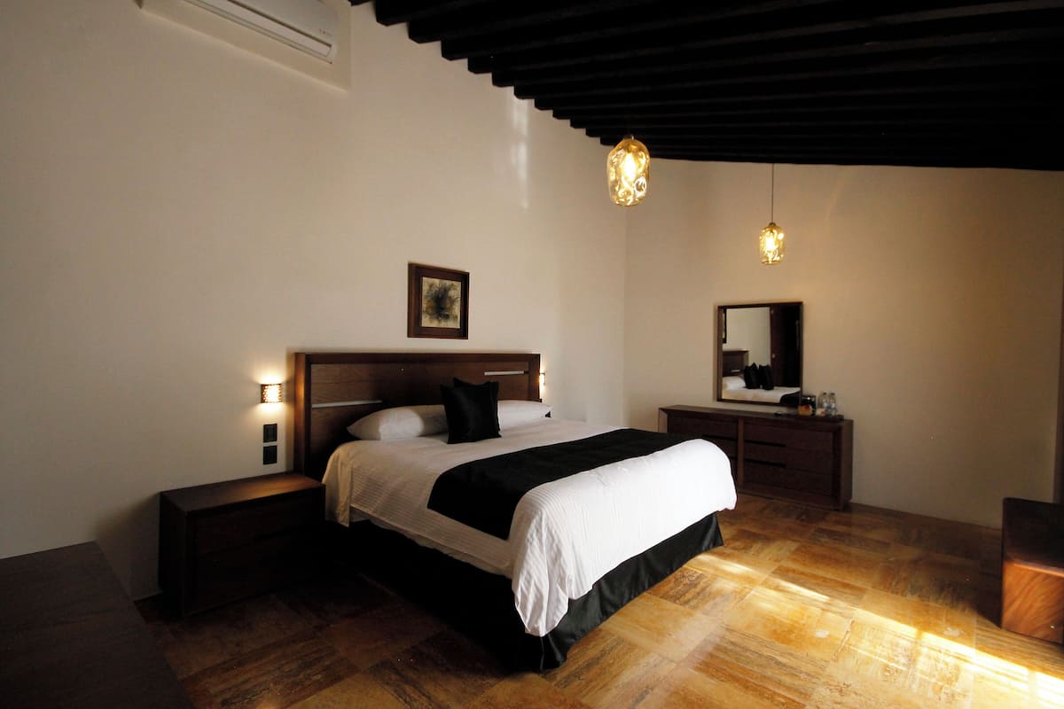 A bedroom with a bed, bedside tables, a nightstand, a mirror, and a hanging light fixture.