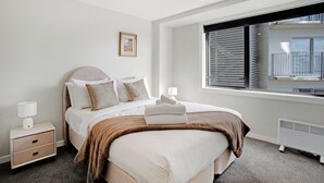 A modern hotel room with a large bed, a nightstand, a window with blinds, and a radiator. - City Skyline Apartment near Myers Park (Auckland)
