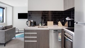A modern kitchen with grey cabinetry, a black tiled backsplash, a built-in oven, and a dishwasher. - City Skyline Apartment near Myers Park (Auckland)
