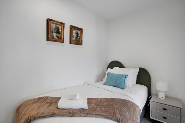 A neatly made bed with a brown blanket, white pillows, and a blue accent pillow. There are two framed pictures on the wall above the bed. - City Skyline Apartment near Myers Park (Auckland)