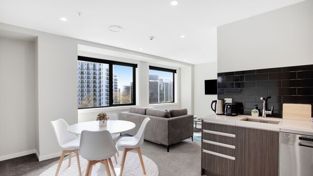 A modern kitchen with a black backsplash, stainless steel appliances, and a dining area with a round table and chairs. - City Skyline Apartment near Myers Park (Auckland)