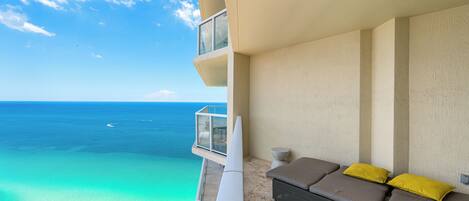 A balcony with a view of the ocean, a sofa with cushions, and a small table.
