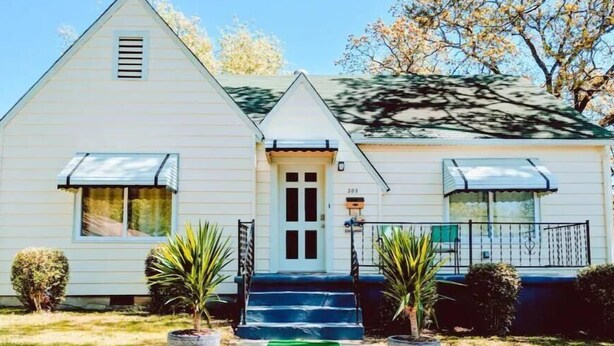 A two-story house with a front porch, a mailbox, and a small garden with potted plants.