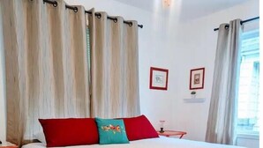 A bedroom with a large bed, red and teal pillows, and beige curtains.