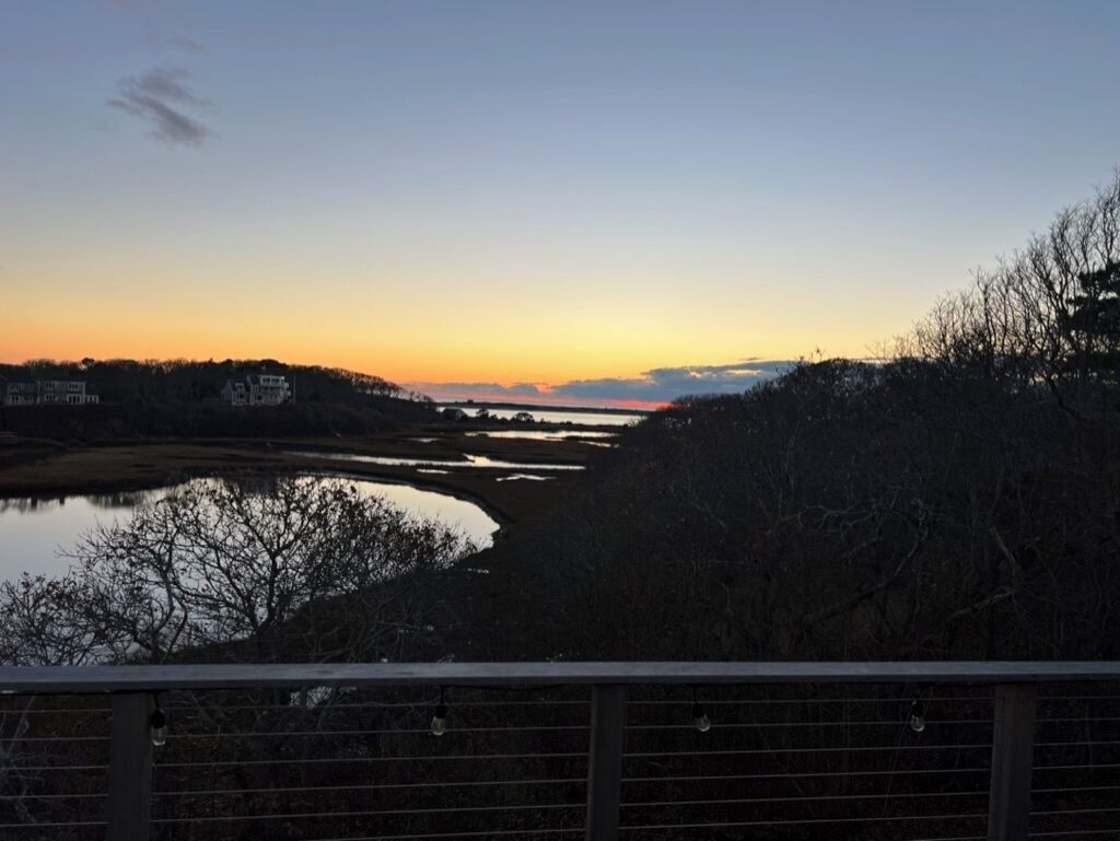 Une vue sur le coucher de soleil depuis un pont, avec une étendue d'eau et des arbres au premier plan.