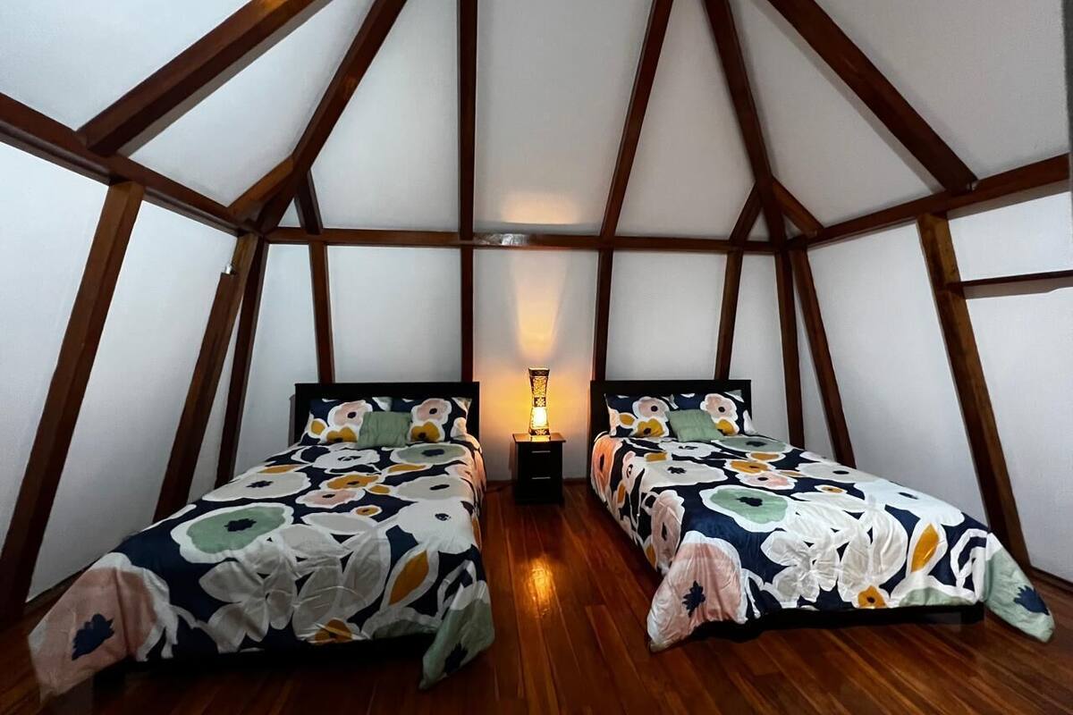 Ein kleines, dreieckiges Schlafzimmer im Dachgeschoss mit zwei Betten, Holzbalken und einem Nachttisch mit Lampe.
