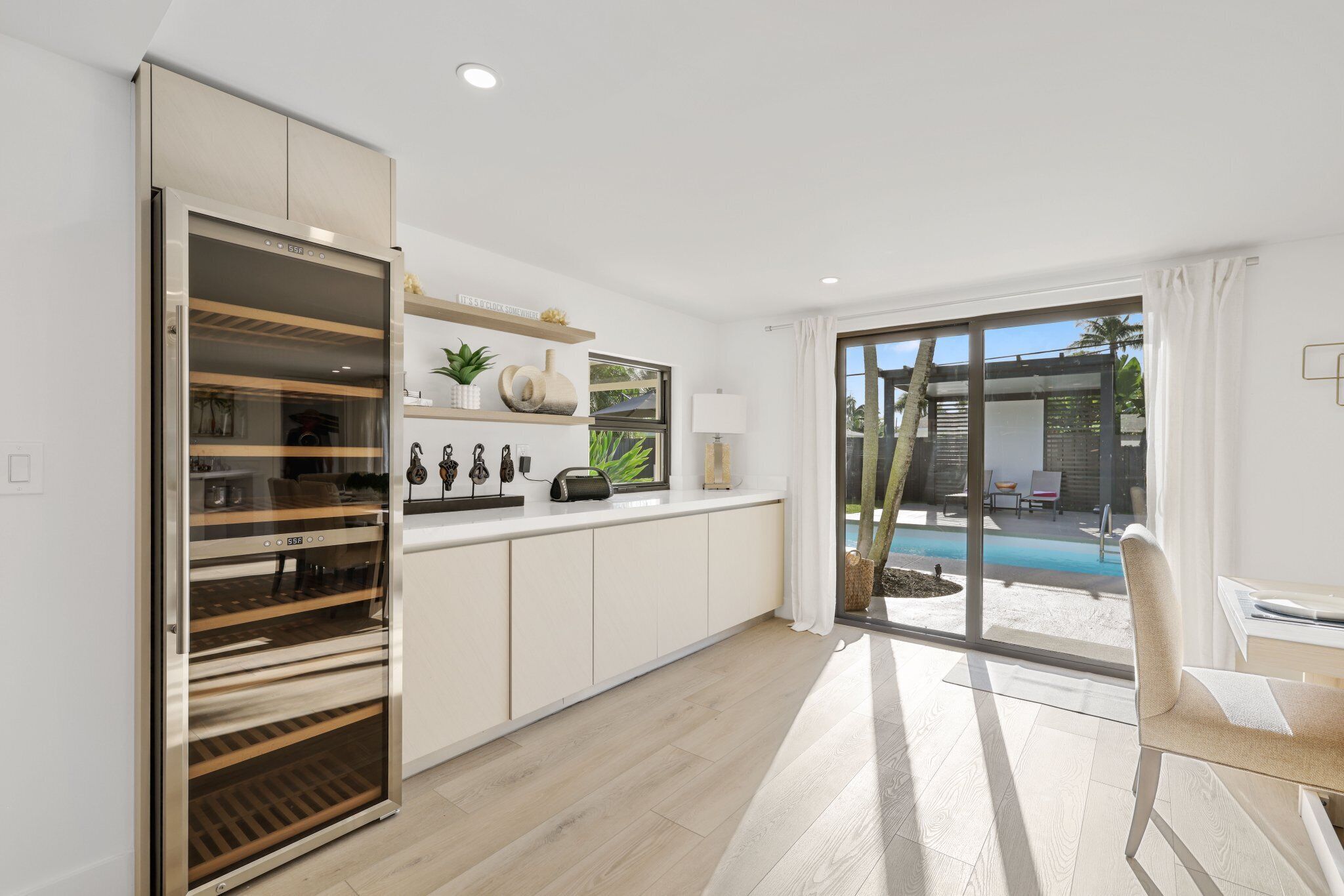 Una cocina moderna con horno empotrado, un comedor con mesa y sillas, y vista a una piscina a través de puertas de cristal grandes.