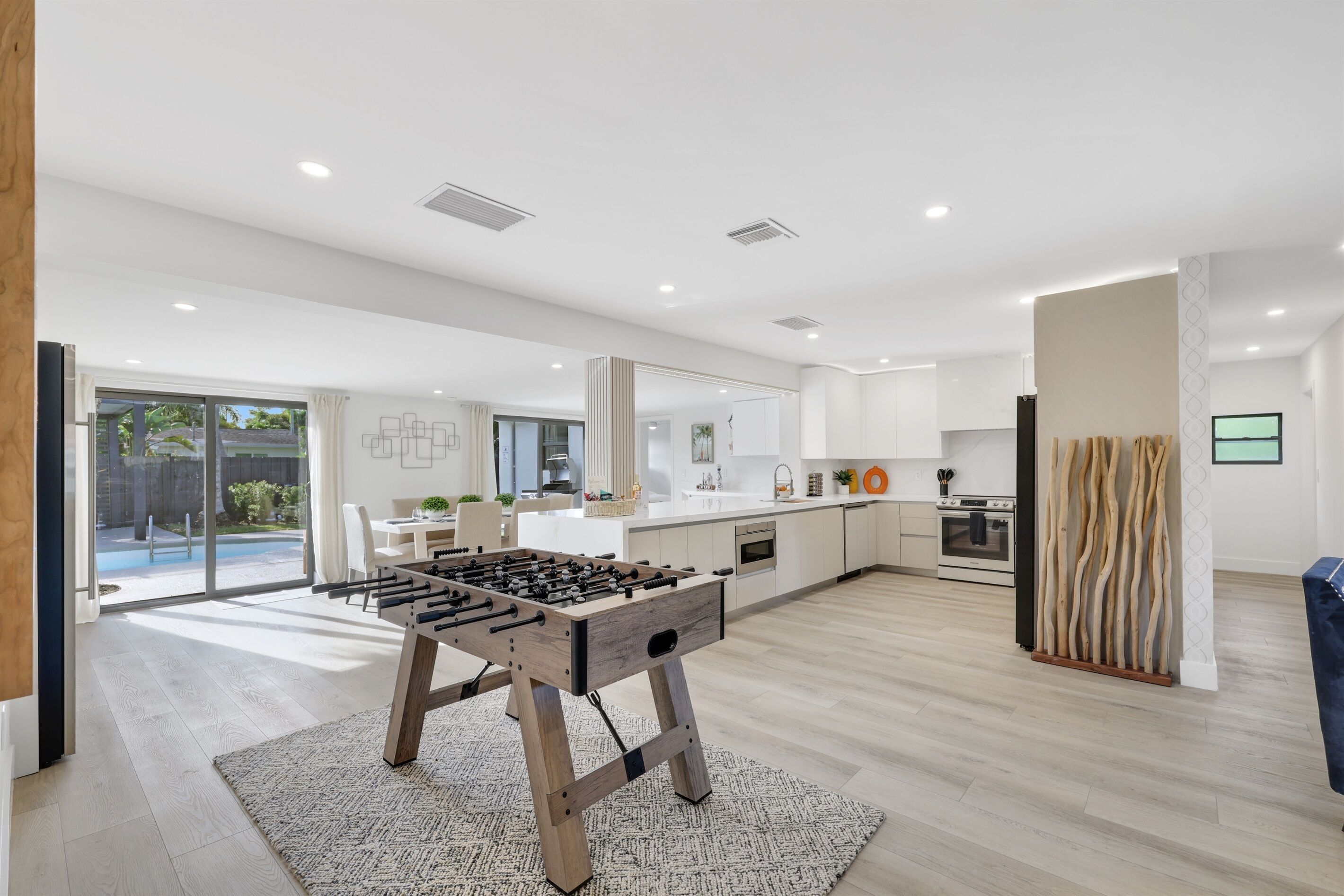 A modern kitchen with a foosball table, a dining area, and a large sliding glass door leading to a patio.