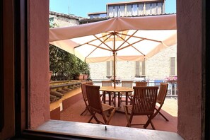 Eine Terrasse mit Tisch und Stühlen unter einem großen Sonnenschirm, umgeben von Kübelpflanzen und einer Steinmauer.