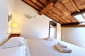 A bedroom with a wooden ceiling, a bed with white linens, a nightstand with a lamp, and a window with a view.