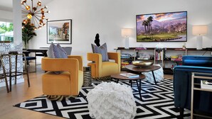 A modern living room with a large flat-screen TV, a unique chandelier, and a cozy seating area with a patterned rug. - Stylish Desert Oasis - Private Pool & Spa, 3BR/2BA Luxury Stay close to Downtown (Palm Springs)
