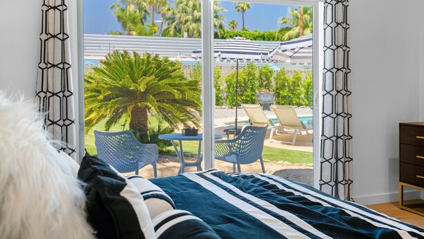 A bedroom with a bed, a view of an outdoor pool area, and a dining table with chairs. - Stylish Desert Oasis - Private Pool & Spa, 3BR/2BA Luxury Stay close to Downtown (Palm Springs)