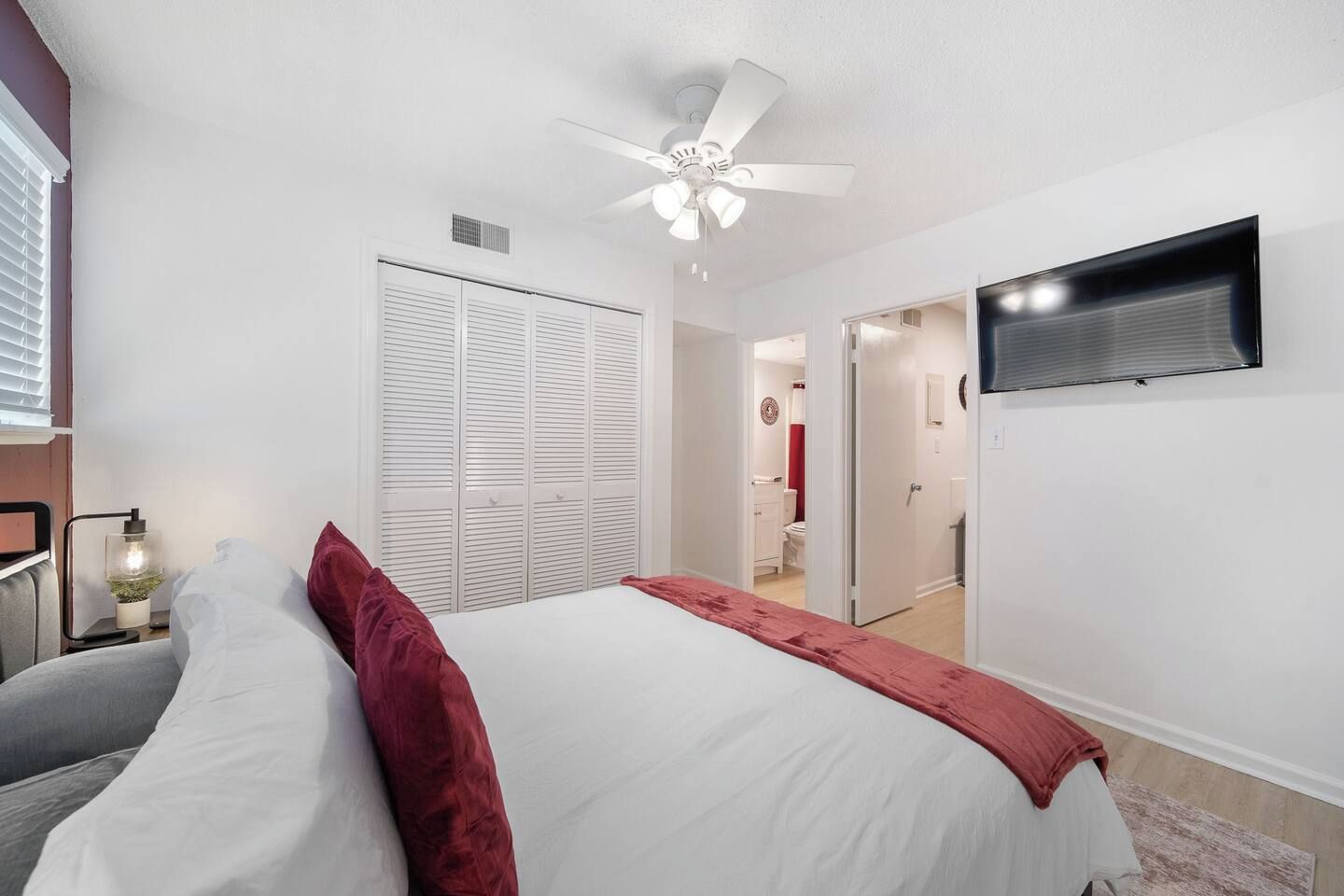 A bedroom with a bed, a ceiling fan, a TV mounted on the wall, and a closet.
