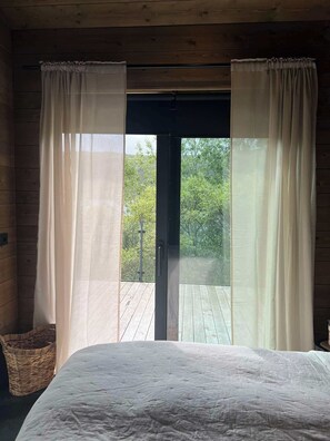 A bedroom with a bed, wooden walls, and a view of trees through a glass door.