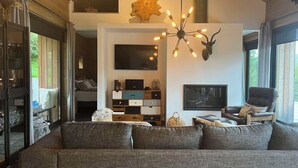 A modern living room with a large gray sofa, a mounted TV, and a unique ceiling light fixture. - Riverside Cottage (Skorradalshreppur)