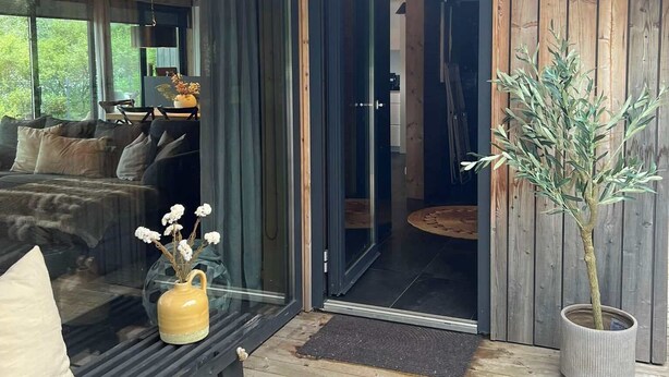 A wooden exterior with a glass door leading to a living area with a sofa and a coffee table. - Riverside Cottage (Skorradalshreppur)