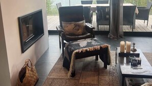 A cozy living room with a fireplace, comfortable seating, a coffee table, and a view of a lake. - Riverside Cottage (Skorradalshreppur)