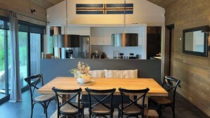 A modern dining area with a wooden table and chairs, a hanging light fixture, and a view of the outdoors. - Riverside Cottage (Skorradalshreppur)